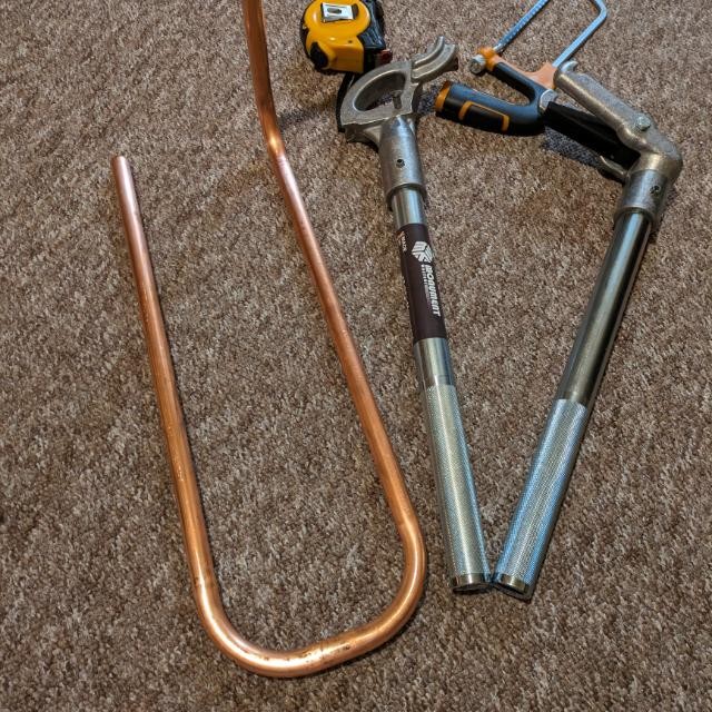 Freshly bent copper pipe beside a pipe bender and tape measure